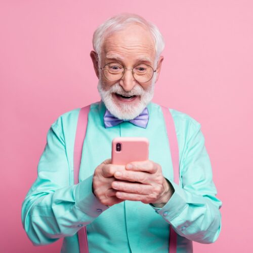 Portrait of surprised crazy shocked old man use smartphone read, social media news enjoy comments wear teal outfit purple violet bow tie isolated pastel pink color background